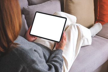 Mockup image of a woman holding digital tablet with blank desktop screen while lying on a sofa at...