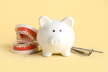 Piggy bank, jaw model and dental tools on beige background