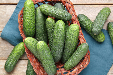 Wicker basket with fresh cucumbers on wooden background