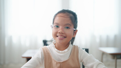 Close up smiling face of excellent Asian student schoolgirl in glasses looking at camera while sitting in classroom at school. Confident Asian student schoolgirl. Education concept