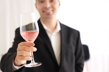 Young sommelier with glass of pink wine in kitchen, closeup