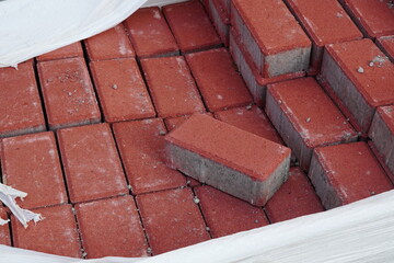 Stack of red concrete pavers for paving footway stored in raffia bag outdoor