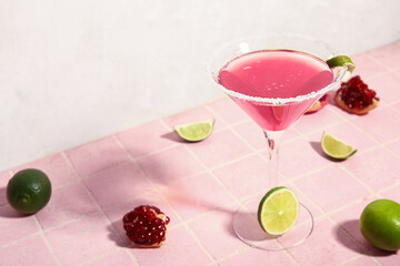 Glass of Cosmopolitan cocktail with lime and pomegranate on pink tile table