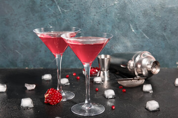 Glasses of Cosmopolitan cocktail with pomegranate and ice cubes on black table