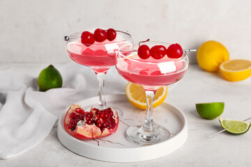 Glasses of Cosmopolitan cocktail with cherries and pomegranate on white background