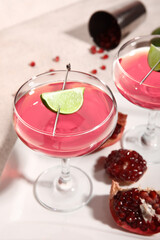 Glass of Cosmopolitan cocktail with lime and pomegranate on white background