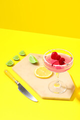 Glass of Cosmopolitan cocktail with cherries and lemon on yellow background