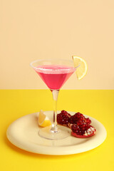 Glass of Cosmopolitan cocktail with lemon and pomegranate on yellow background