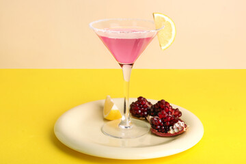 Glass of Cosmopolitan cocktail with lemon and pomegranate on yellow background