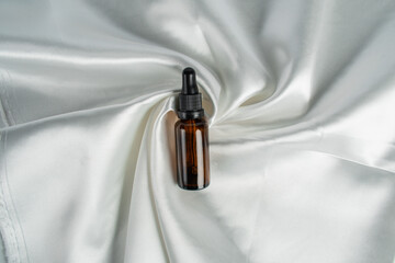 Cosmetic bottles made of dark amber glass on shiny cloth background