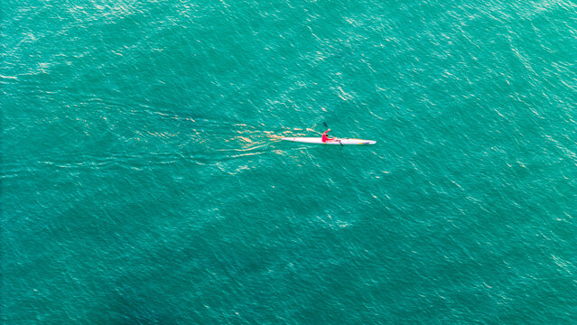 Kayaker paddling across ocean water at sunrise - Powered by Adobe