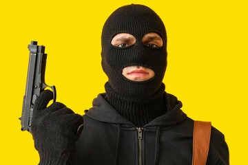 Male thief with gun on yellow background