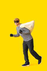 Male thief with bag on yellow background