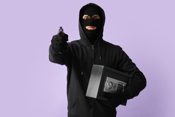 Male thief with gun and safe box on lilac background