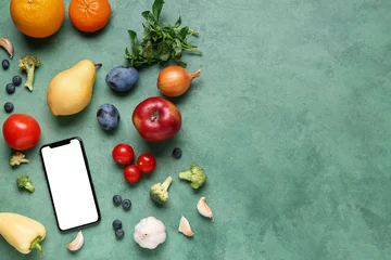 Rolgordijnen Mobile phone with fresh vegetables and fruits on green background. World Vegan Day concept © Pixel-Shot