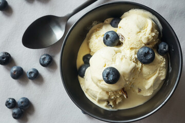 Ice cream with fresh blueberries in a dark plate next to a spoon