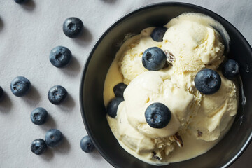 Ice cream with fresh blueberries in a dark plate next to a spoon