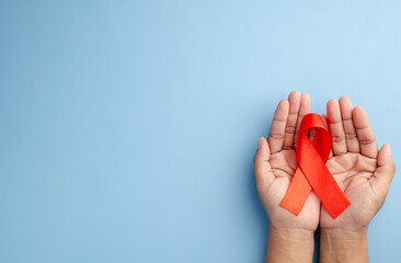 Healthcare and medicine concept - female hands holding red AIDS awareness ribbon on blue background
