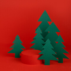 Christmas background - one red cylinder podium mockup for presentation cosmetic products, gifts, goods, green paper spruces in cartoon art style, copy space, square. New year template for advertising.