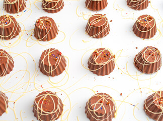 Brown chocolate sweets with white chocolate lines, on a white tray