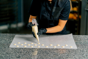 A confectioner squeezes chocolate from a pastry bag in the form of natural candies onto parchment...