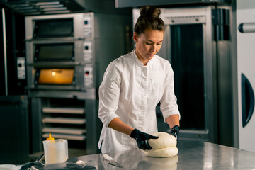 professional female baker carefully kneads the dough for baking fresh bread in cozy bakery