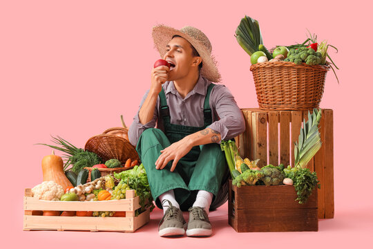 Male farmer with fresh vegetables eating apple on pink background - Powered by Adobe