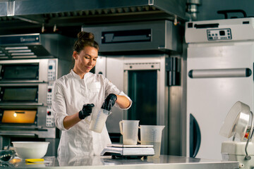 Female chef pouring water into a measuring glass standing on a kitchen scale in professional kitchen