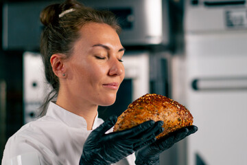 Portrait of a girl in a professional bakery kitchen who inhales aroma of freshly baked bread and...