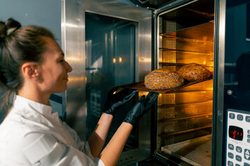A female baker wearing gloves takes out a baking sheet with freshly baked hot bread from oven