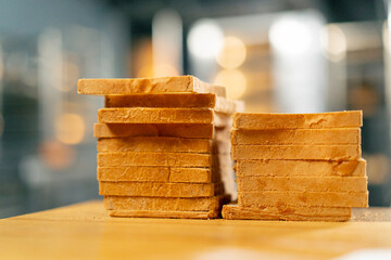 Close-up shot of a loaf of bread cut into toasts standing on a wooden board on kitchen surface - obrazy, fototapety, plakaty