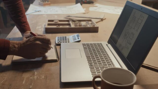 Close-up shot of hands of unrecognizable Caucasian man using touchpad on laptop while working at carpentry