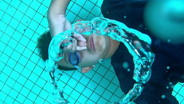 The young boy blows ring bubbles underwater in the swimming pool. 4K in slow motion