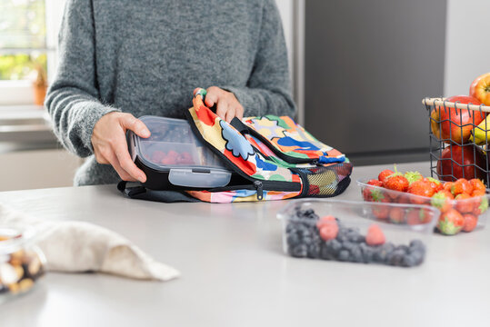 Mom packs a lunch box with snacks lunch in a school backpack in the kitchen.