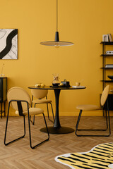 Creative composition of dinning room interior with mock up poster frame, round table, stylish chair, yellow wall, black rack, lemon, patterned carpet and personal accessories. Home decor. Template.