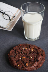 Chocolate chip cookies with a glass of milk on the background of an open book on a gray table