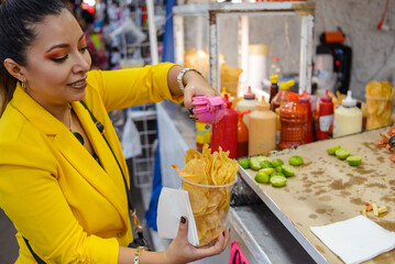Woman adding lime juice on potato chips at a fast food stand in Mexico.