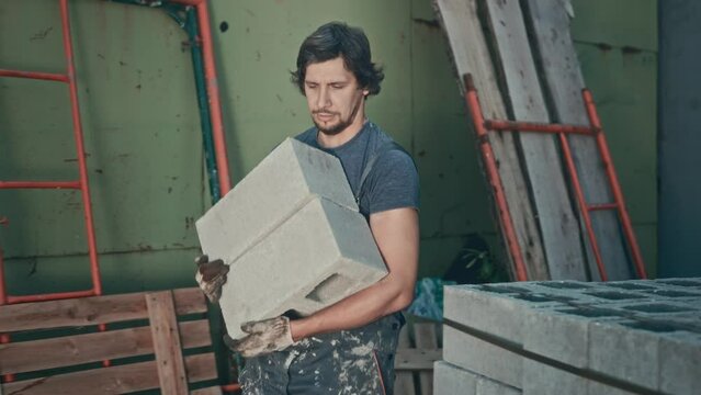 Low-skilled construction labor. A man works as a loader and carries heavy building blocks.