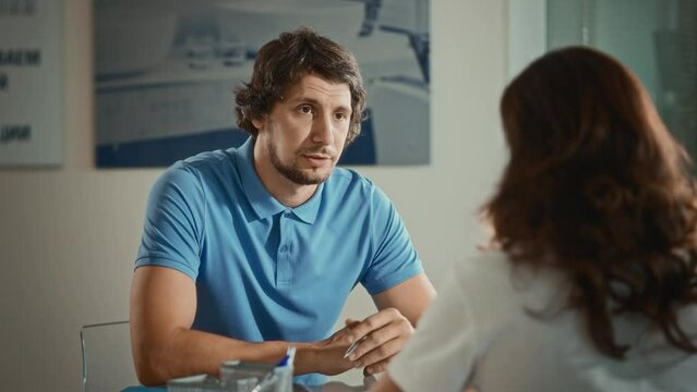 A man dressed in a polo at an interview in the office. A woman meets with a potential new employee to discuss contract terms and salary.