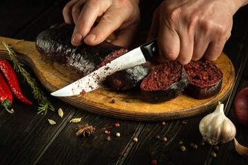 Male hands use a knife to cut blood sausage on a cutting board. Preparing a national dish on the...