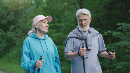 Two sporty old pensioners enjoy nordic walk in green nature wood park. Romantic family hikers date....