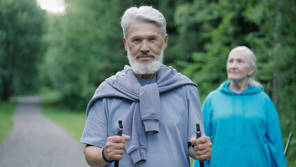 Senior hiker couple look camera green forest background. Aged adult grandparents. Handsome serious...