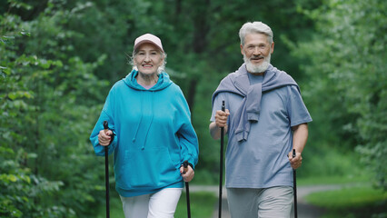 Elder family hikers pair fun stroll. Two happy old sportsman enjoy romantic date. Old sporty couple nordic walk poles green nature forest park. Senior people sport fit workout. Grandparents joy smile.