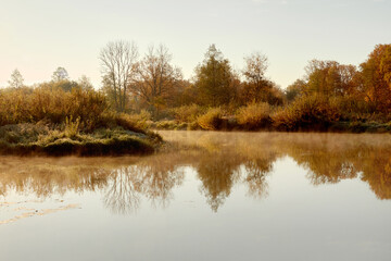 Small river in an autumn woodland. Morning fog over the river.