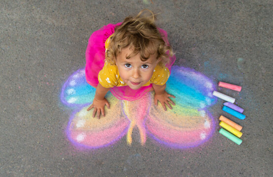 A child draws a butterfly on the asphalt with chalk. Selective focus.