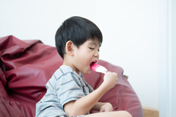 An Asian boy is eating delicious ice cream in a chair.