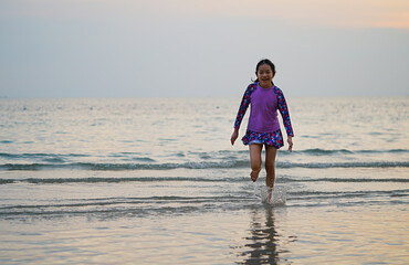 Portrait Asian little girl running on the beach, splash seawater, running direct to camera, sunset time, landscape image with space for copy and design.