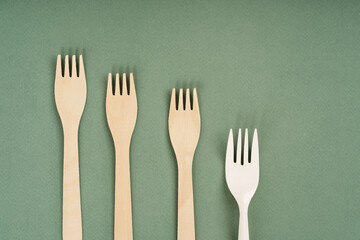 Wooden forks, spoons and one plastic fork on a green background. Eco-friendly disposable tableware. Refusal of plastic. The concept of caring for nature.