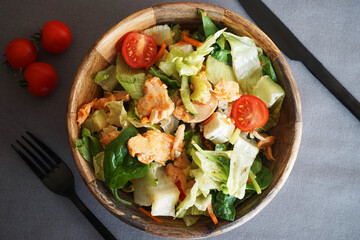 Vegetable salad with chicken and cheese next to a knife and fork on a gray background