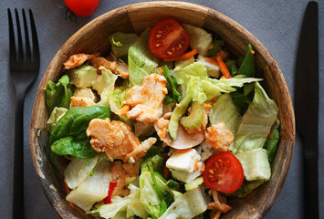 Vegetable salad with chicken and cheese next to a knife and fork on a gray background